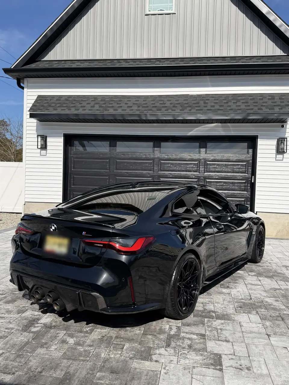 Black BMW M4 Competition with mirror-gloss paint in front of a garage