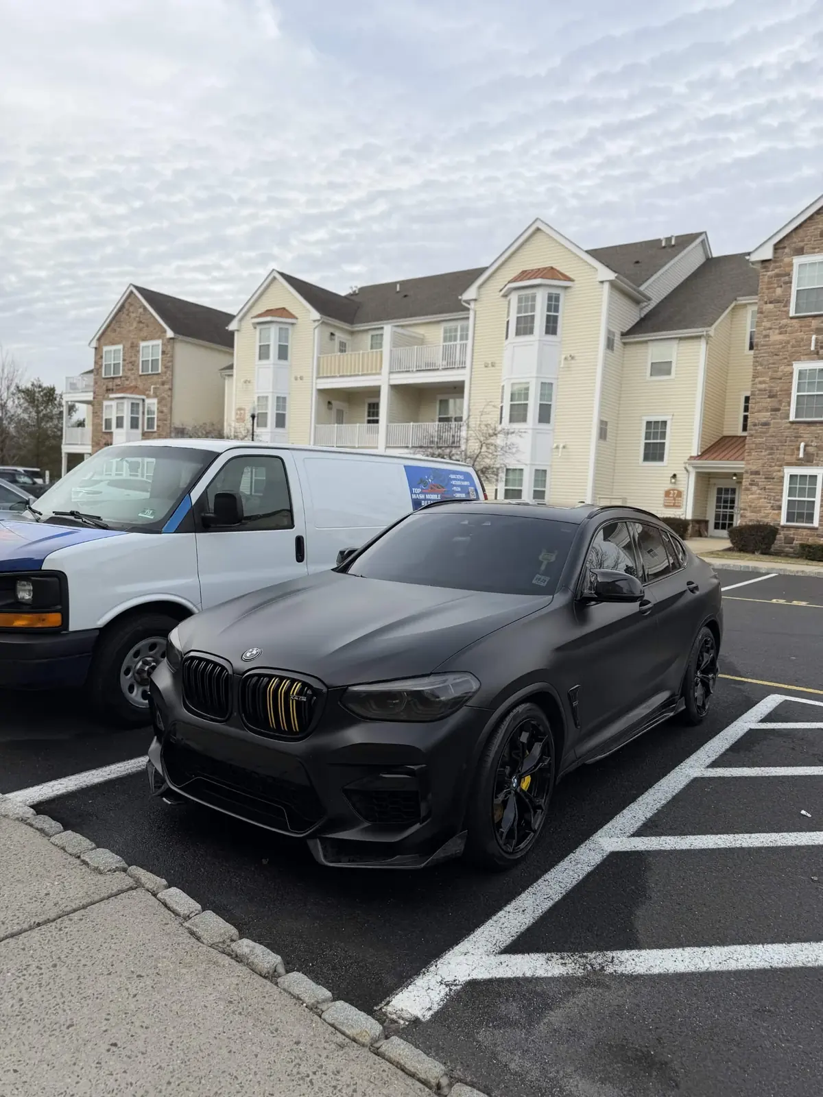 Satin black BMW X4 M Competition beside the Top Wash van